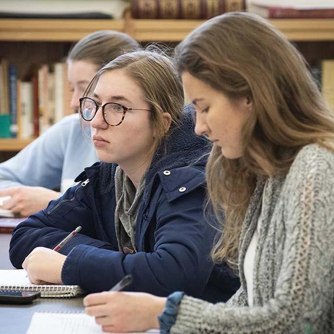 Two female students taking notes during lecture